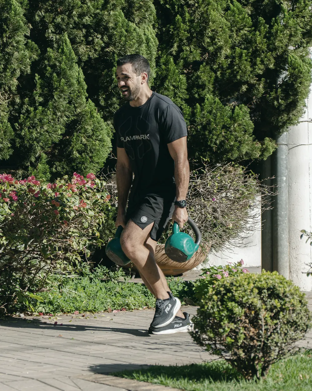 Bruno carregando dois kettlebells em treino ao ar livre